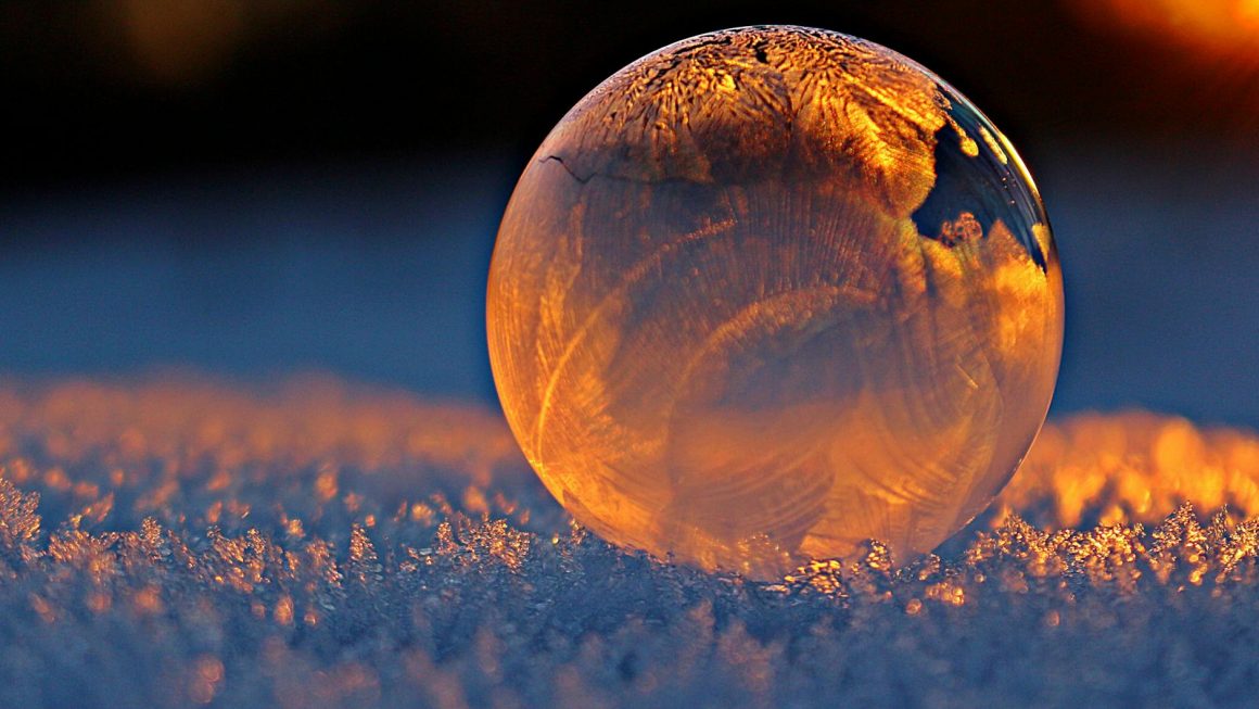 La photo capture une sphère de glace posée sur un sol enneigé, baignée par la lumière chaude d'un coucher ou d'un lever de soleil. Cette image pourrait illustrer un article "Comment les écrivains représentent-ils l'hiver et la neige ?", en utilisant la sphère comme métaphore de la contemplation et de la réflexion, souvent présente dans la littérature pour décrire les paysages hivernaux. La lumière qui illumine la sphère pourrait symboliser l'espoir ou la clarté qui émerge dans le froid de l'existence humaine.