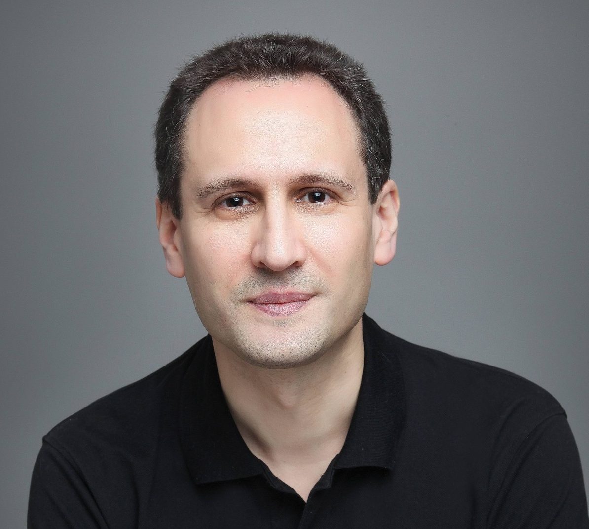 Portrait de William Alexandre, auteur du livre Perdre son job, encaisser et rebondir, vêtu d’un polo noir, les bras croisés et arborant une montre élégante. Il pose avec un léger sourire, regardant directement l’objectif