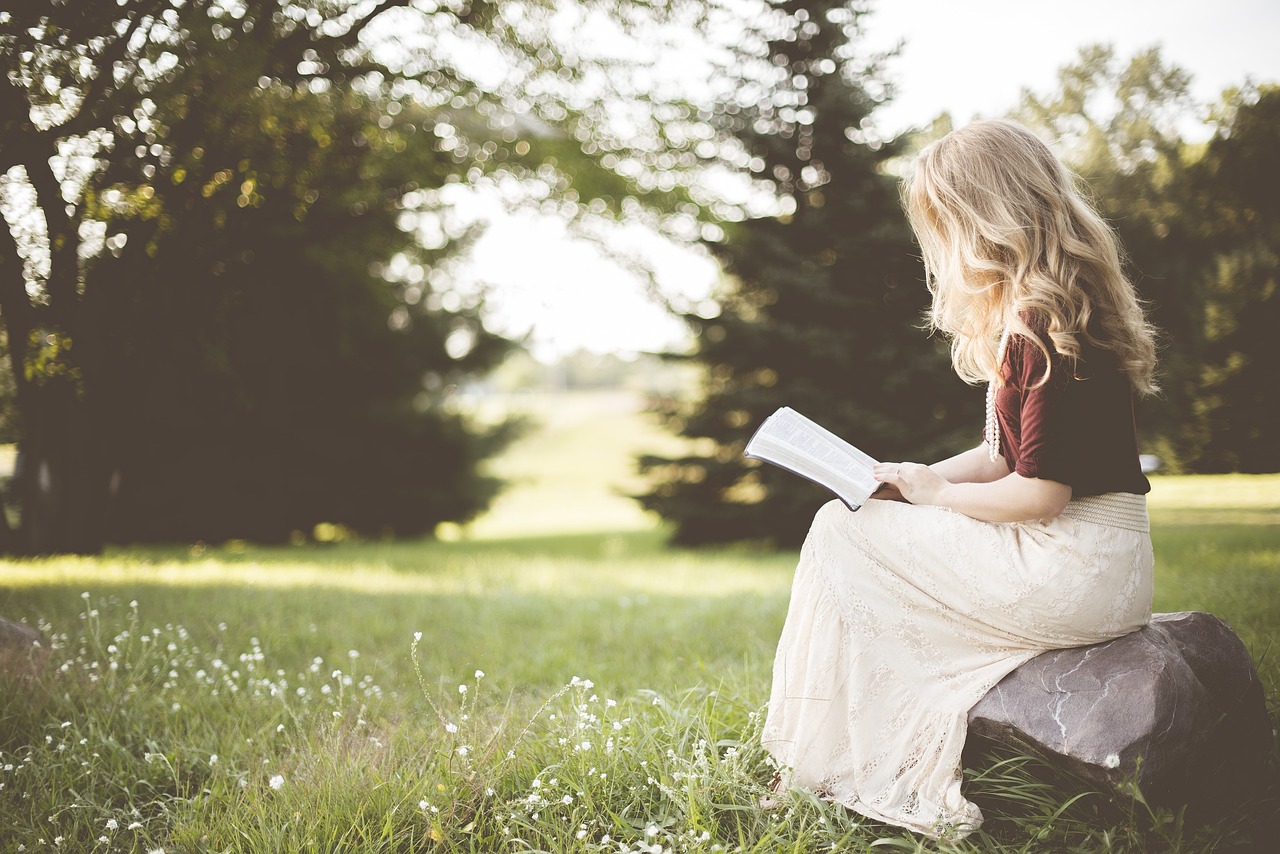 Une jeune femme blonde lisant attentivement sur un rocher, inspirée par ses résolutions littéraires pour la rentrée dans un parc paisible.