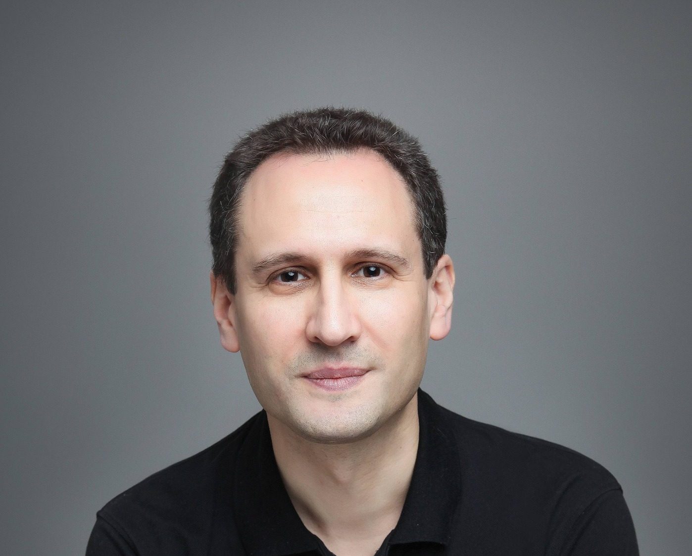 Portrait de William Alexandre, auteur, posant pour une interview. Il porte un polo noir et une montre en métal, avec un fond gris uni.