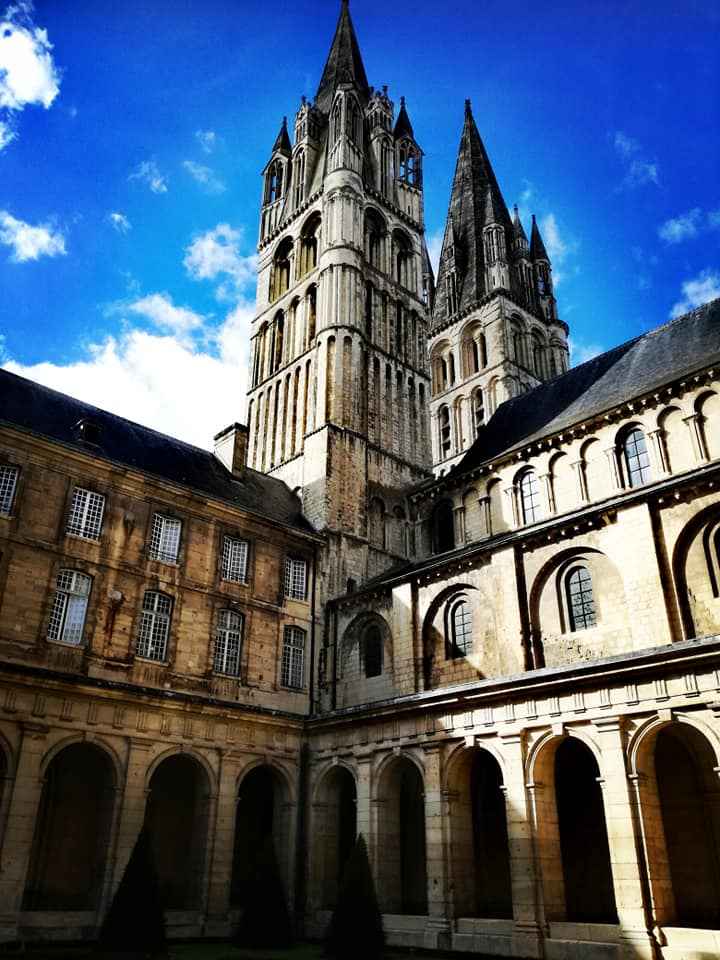 Vue majestueuse de l'Abbaye-aux-Hommes à Caen, mettant en valeur son architecture gothique et son cloître sous un ciel bleu éclatant. Cette image reflète aussi les légendes et les mystères de Caen.
