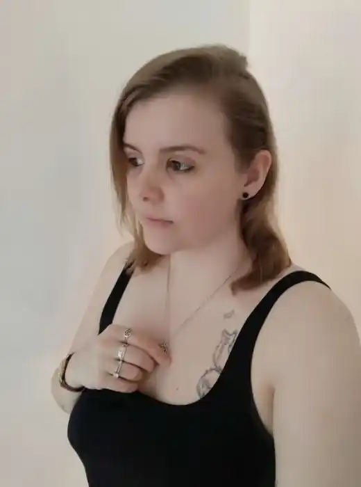 Portrait d'Elodye H. Fredwell, cliente satisfaite, portant un débardeur noir, avec un regard doux et une main posée sur son collier.