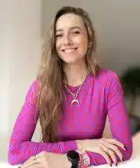 Portrait d'Anna Vasseliva, cliente rayonnante, portant un haut rose à motifs, assise et souriante, témoignant de son expérience positive avec Charlène Rédac’.