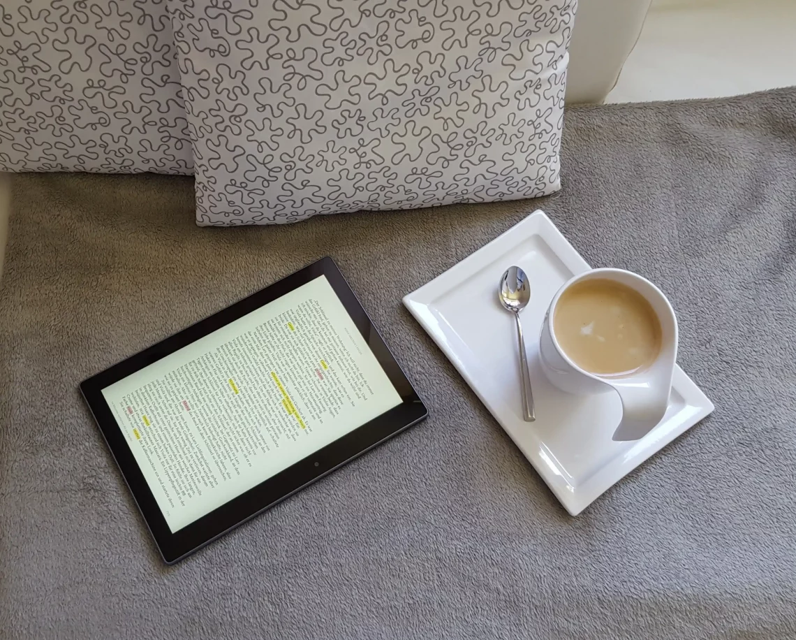 Auteur autoédité qui lit et annote un ebook sur tablette avec un café — marketing littéraire et lecture numérique