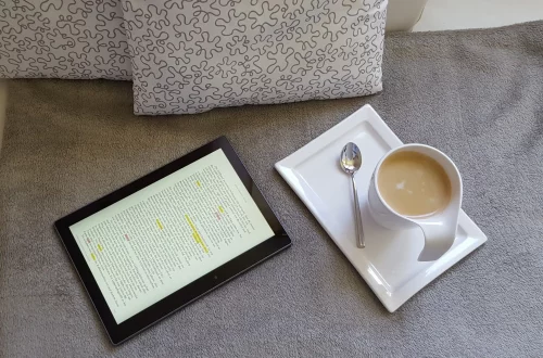 Auteur autoédité qui lit et annote un ebook sur tablette avec un café — marketing littéraire et lecture numérique