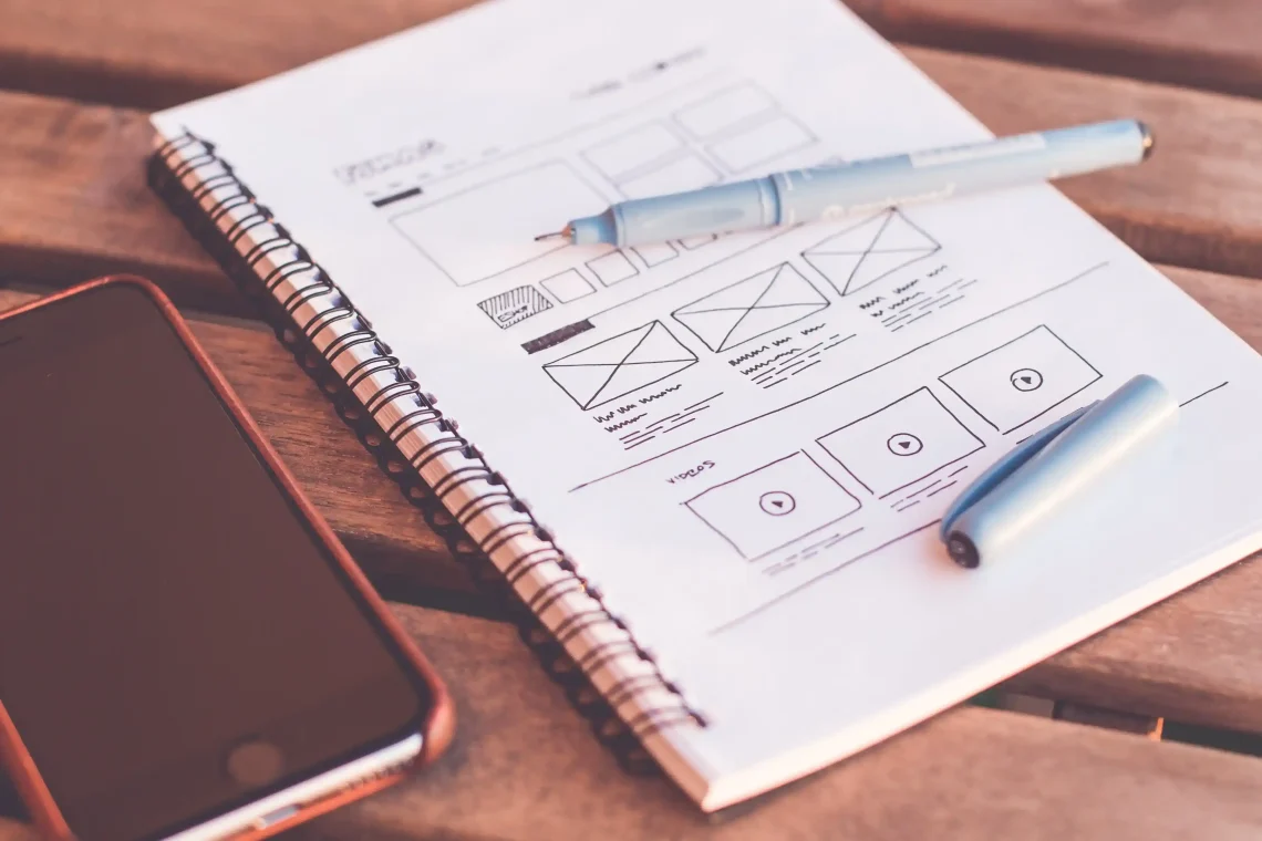Carnet de croquis avec wireframe de site web dessiné à la main, smartphone et stylos - gagner en visibilité sur le web en tant qu'auteur (visibilité web auteur).